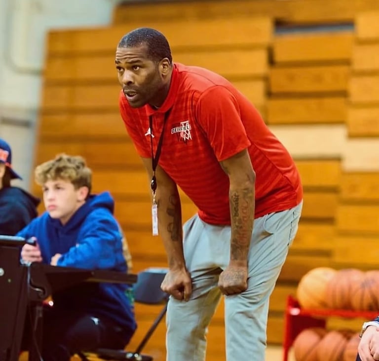 Coach in red shirt instructs youth basketball players in a gymnasium during practice