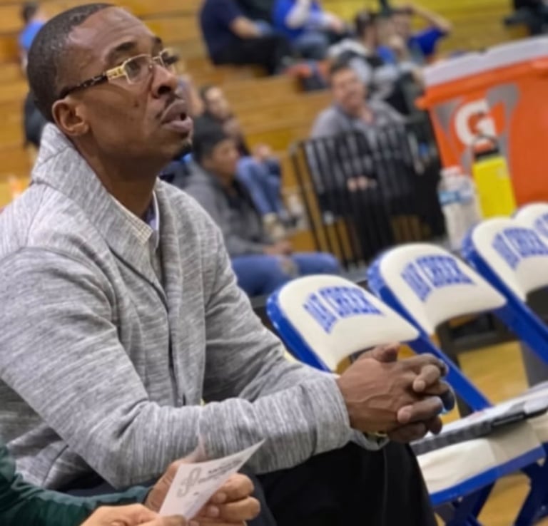 Man wearing glasses and gray shirt sitting in arena bleachers watching game