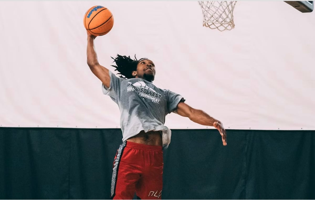 A basketball player shoots the ball toward the hoop while wearing a gray shirt and red shorts