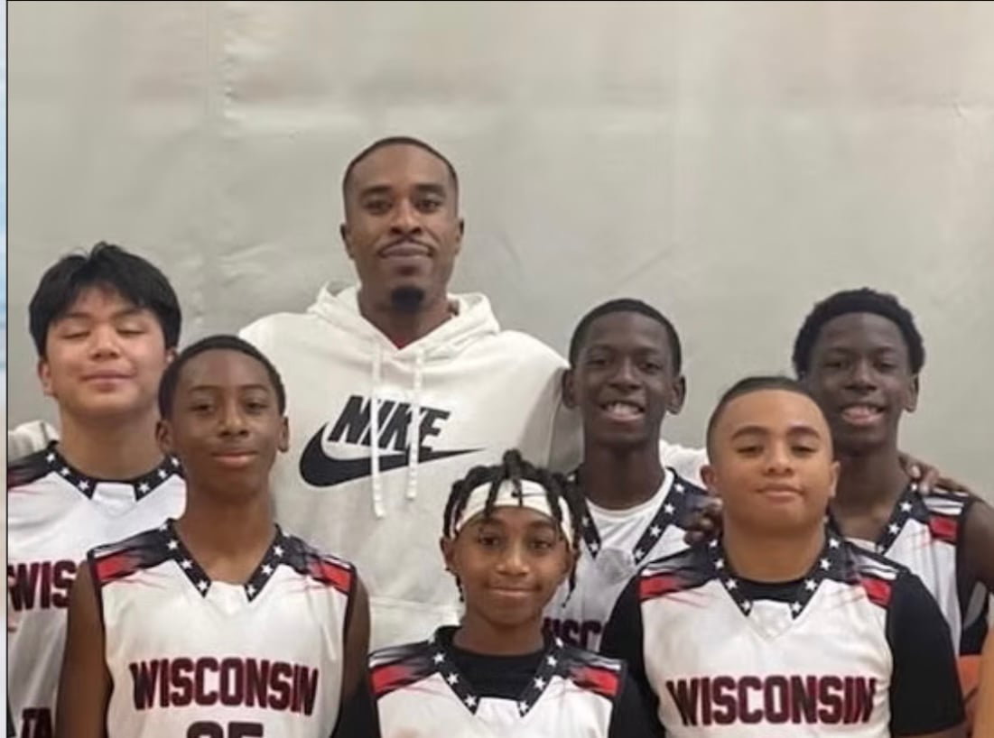 Group photo of six young basketball players in Wisconsin uniforms with an adult coach in a Nike hoodie